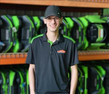 Caden is standing in front of orange shelving with green air movers stacked